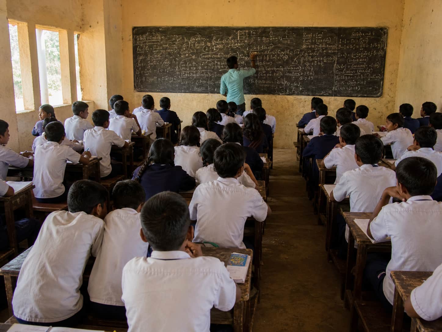 A teacher writing on a messy chalkboard in a large classroom