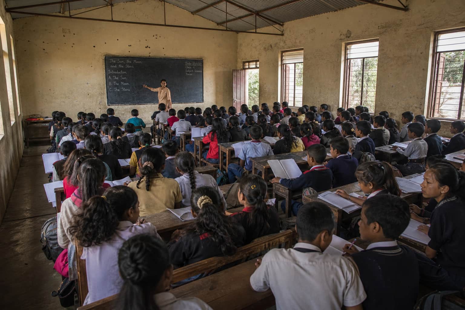 A very large classroom with around 50 students at fixed benches