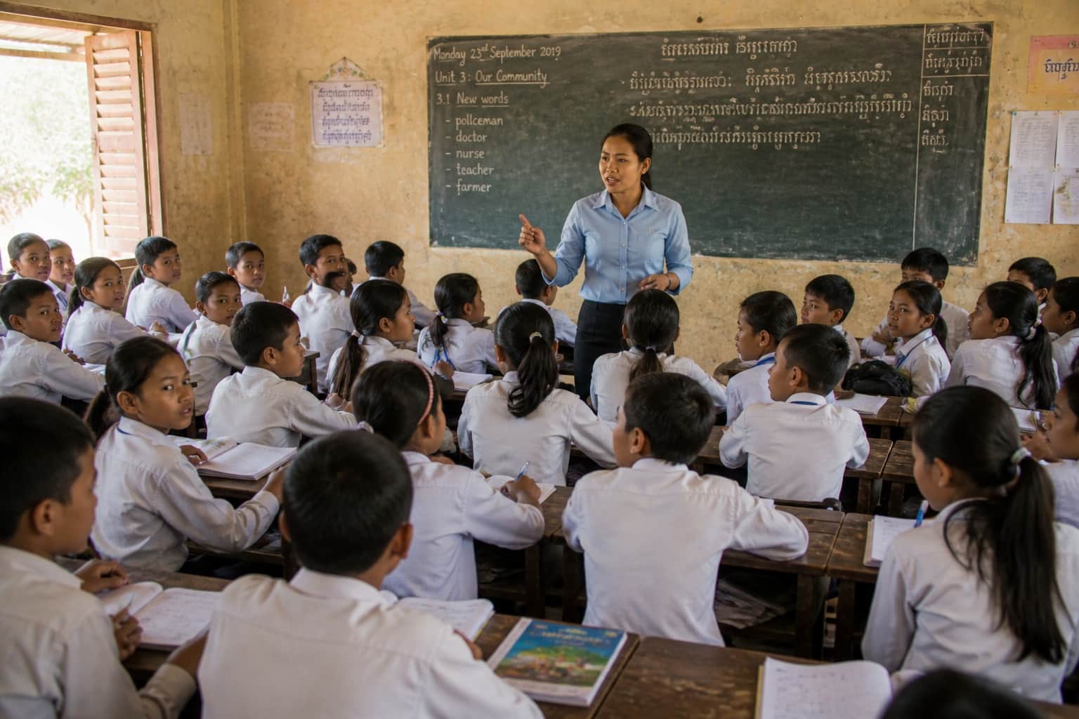 A teacher giving instructions to a large class of students. Some students look attentive while others appear confused.