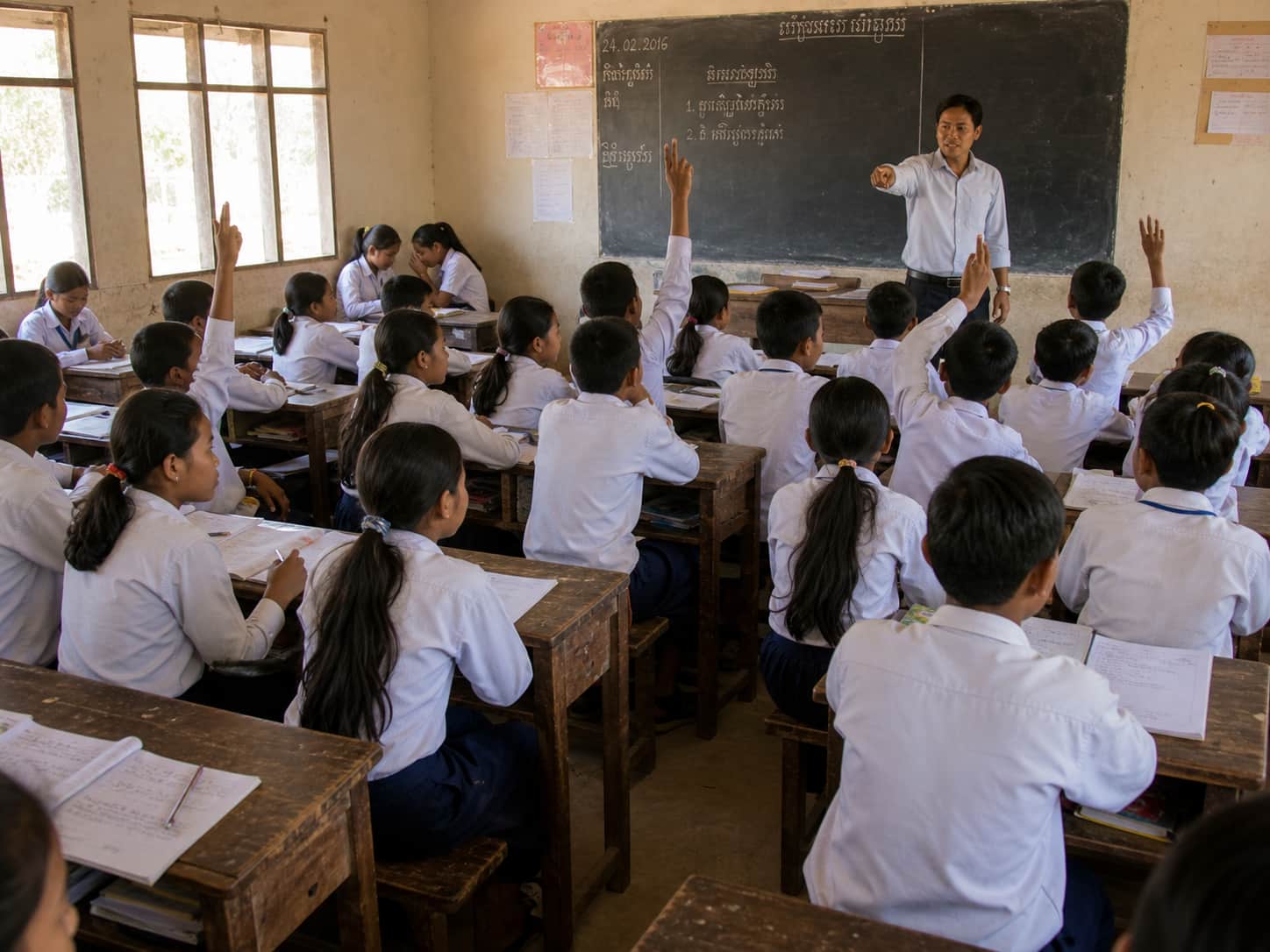 A teacher pointing at a confident student while a shy student in the back looks down