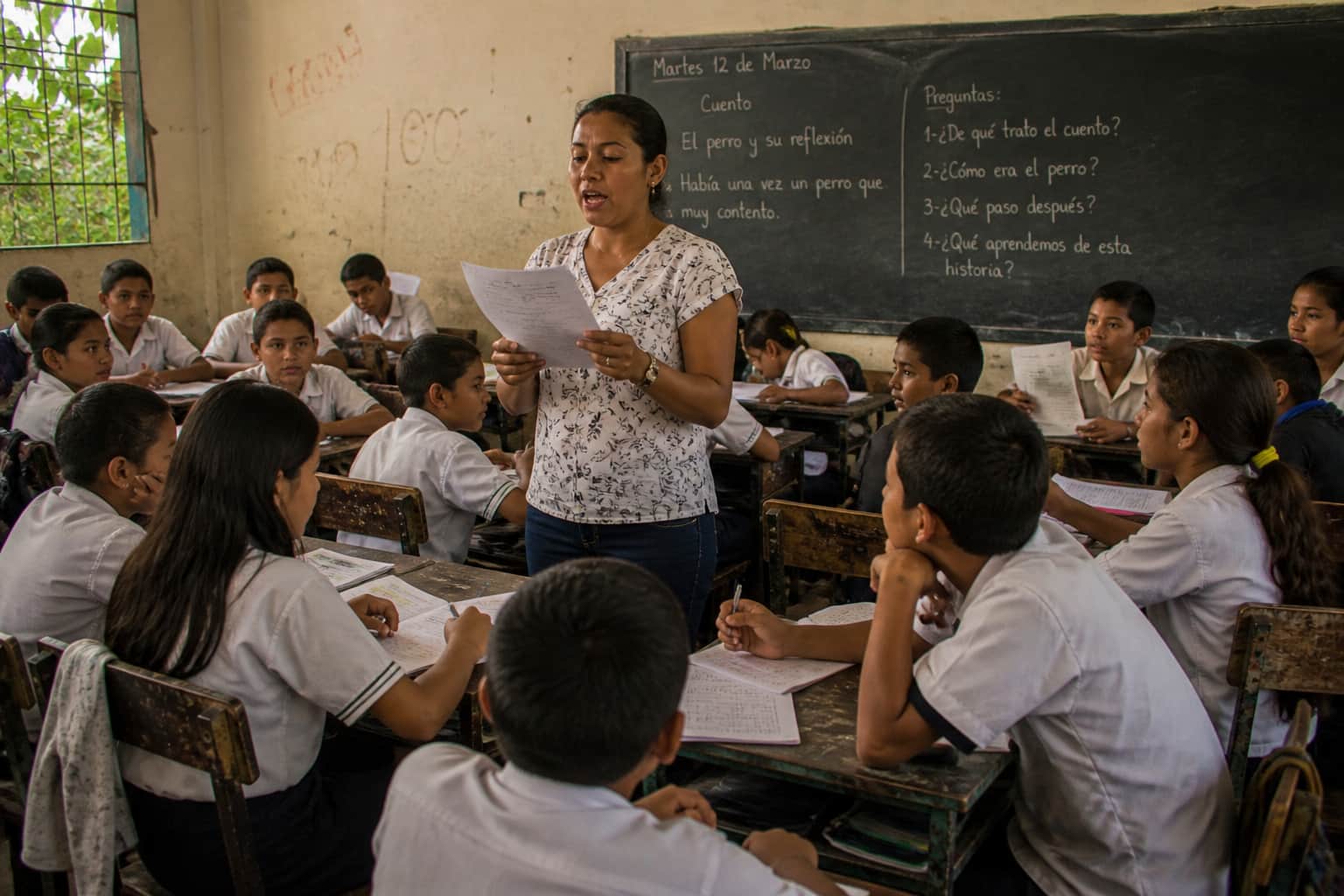 A teacher reading aloud from the middle of the classroom while students listen actively
